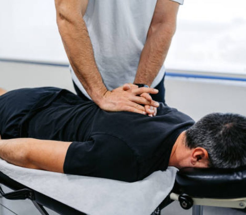 Chiropractor adjusting (cracking) his male client's upper back in his office.